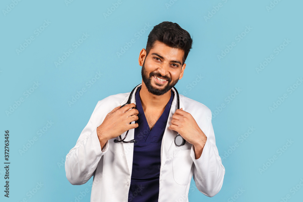 Handsome modern Indian / Asian doctor with stethoscope, in uniform on blue background Handsome modern Indian / Asian doctor with stethoscope, in uniform on blue background