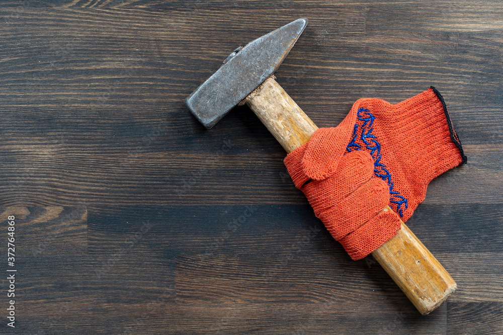 Orange construction gloves in which the hammer is clamped. Tool kit, hammer and work gloves on vintage wooden background, copy space for text