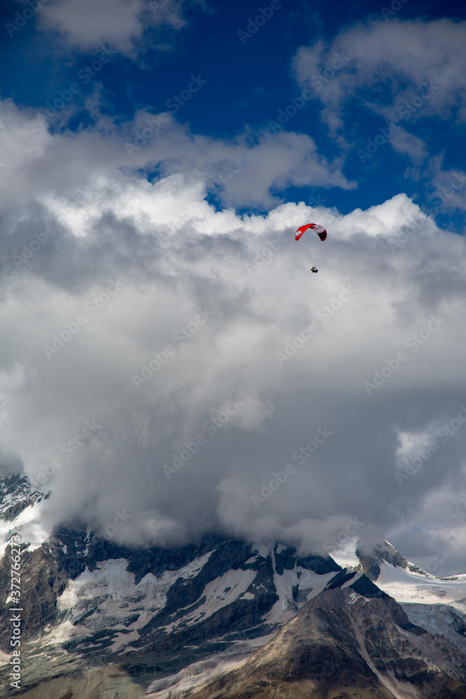Zermatt, Switzerland; A paraglider sails over clouds and mountains near Matterhorn Zermatt, Switzerland; A paraglider sails over clouds and mountains near Matterhorn