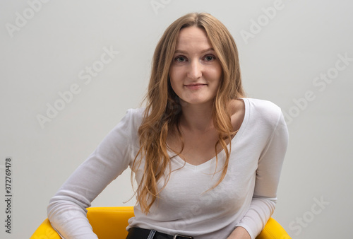 young caucasian woman interested in coversation and looking at camera while sitting in chair, grey background photo