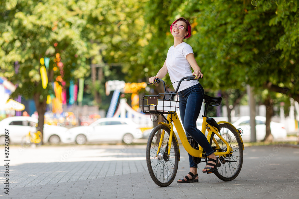 young woman with pink hair walks in the park with a bike eating ice cream in the summer. Environmental mode of transport young woman with pink hair walks in the park with a bike eating ice cream in the summer. Environmental mode of transport
