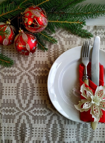 Christmas table setting. a knife and a fork laid out on a linen tablecloth wrapped in a red napkin on a white plate. 