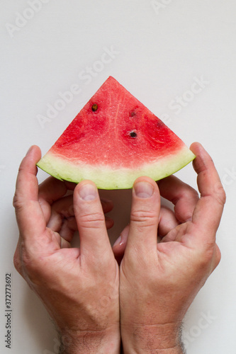 Male hahds holding slice of ripe watermelon on white background, top view photo