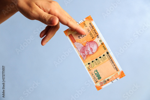 the hand holds 200 rupees bill with two fingers