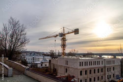Construction of a building on the river Bank against the sunset. Work on the crane. Sunlight, sunset, winter. Beautiful view of the city.