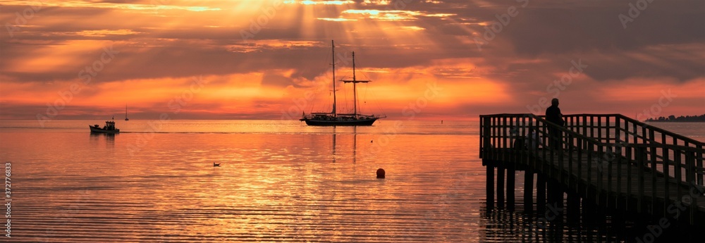 magische Sonnenstrahlen am Steg an der Ostsee mit Segelschiff und Fischerboot