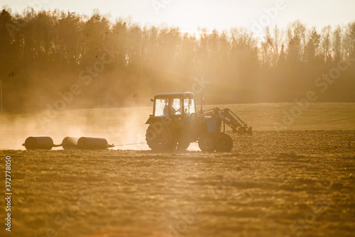 tractor plows the field at sunset. Dust in the air.