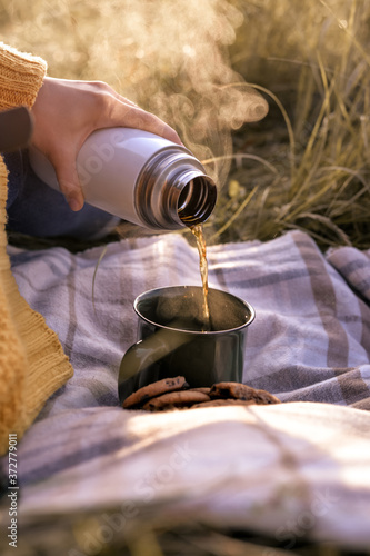 Young girl  in yellow pullover pouring hot drink into the cup outdorr in autumn picnic