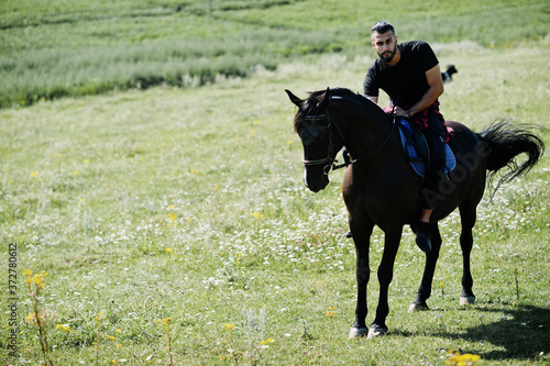 Arab tall beard man wear in black ride arabian horse.