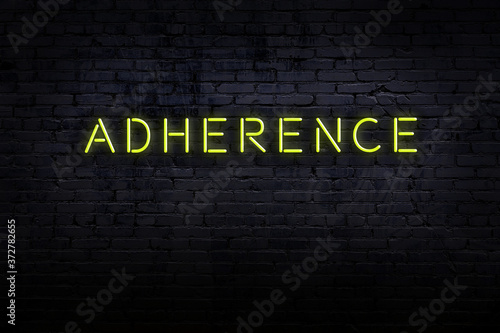 Night view of neon sign on brick wall with inscription adherence
