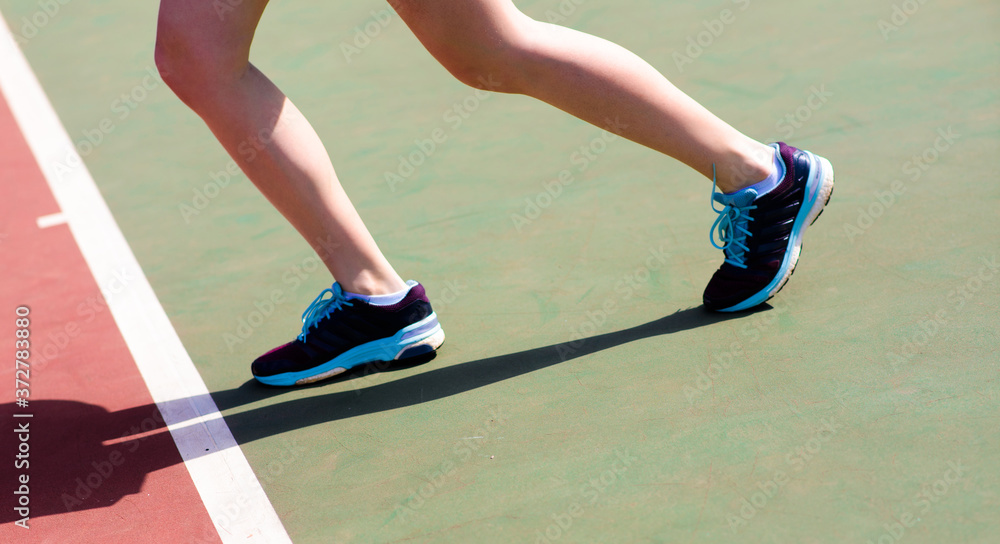 Fototapeta Legs of young girl in a closed tennis court with racket, sport shoes