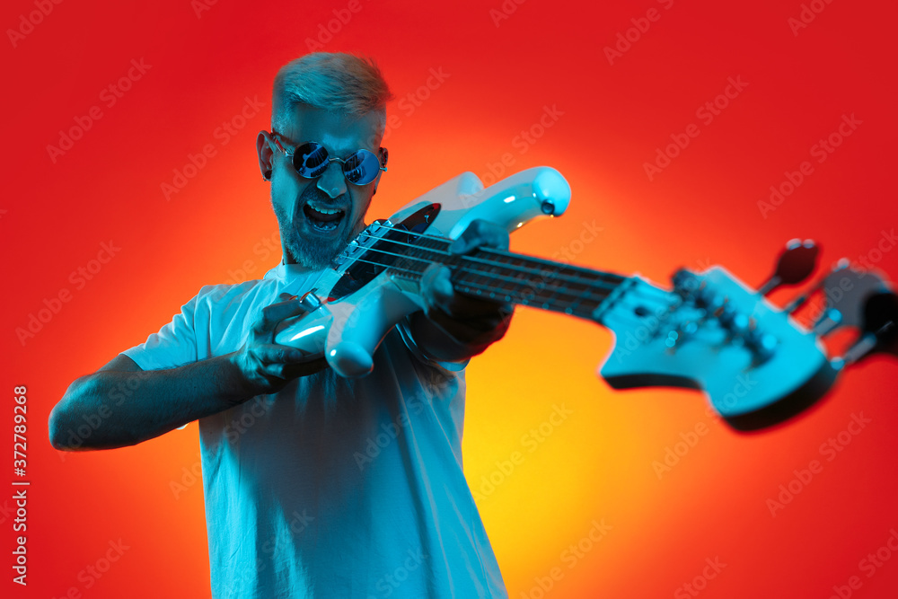 Handsome hipster man holding white bass guitar and screaming in neon lights. Rock music concept. Handsome hipster man holding white bass guitar and screaming in neon lights. Rock music concept.