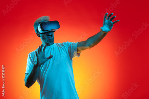 Obraz na płótnie Screaming bearded hipster man with blonde hair wearing virtual reality goggles in studio in neon lights. w salonie