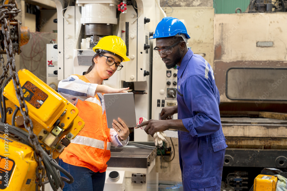 Supervisor, worker with hard hat working in manufacturing factory on business day. Female industrial engineers have to consult with colleagues while using tablet. Concept of workplace gender equality Supervisor, worker with hard hat working in manufacturing factory on business day. Female industrial engineers have to consult with colleagues while using tablet. Concept of workplace gender equality