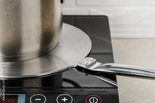 Cookware on a stainless steel heat diffuser plate over a cooktop. Kitchen appliance for induction hob allows to use small diameter or non-ferromagnetic cookware. photo