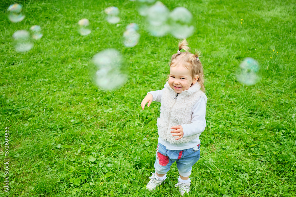 Happy toddler chasing soap bubbles through a summer park. Happy toddler chasing soap bubbles through a summer park.