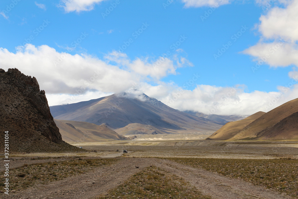 View of the mountains and dramatic sky and a car on the gravel road to Everest Base Camp, Tibet, China View of the mountains and dramatic sky and a car on the gravel road to Everest Base Camp, Tibet, China