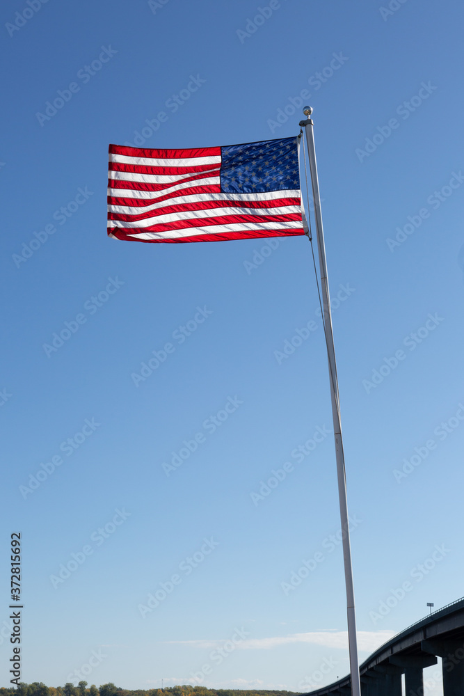 The flag of the United States of America flies in the wind near a bridge