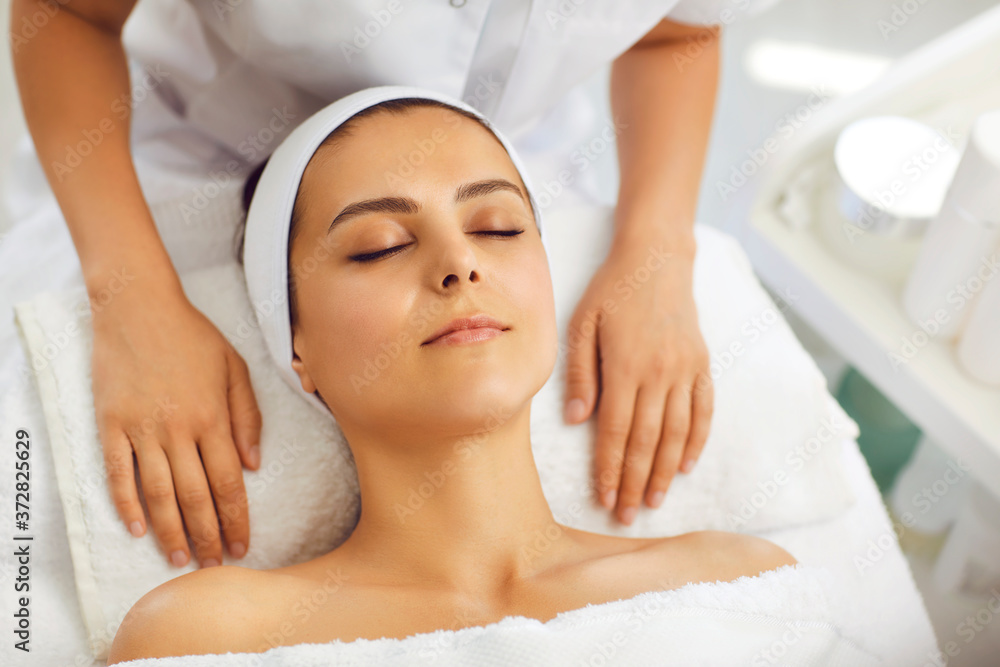 Hands of cosmetologist relaxing on towel near womans face after facial massage