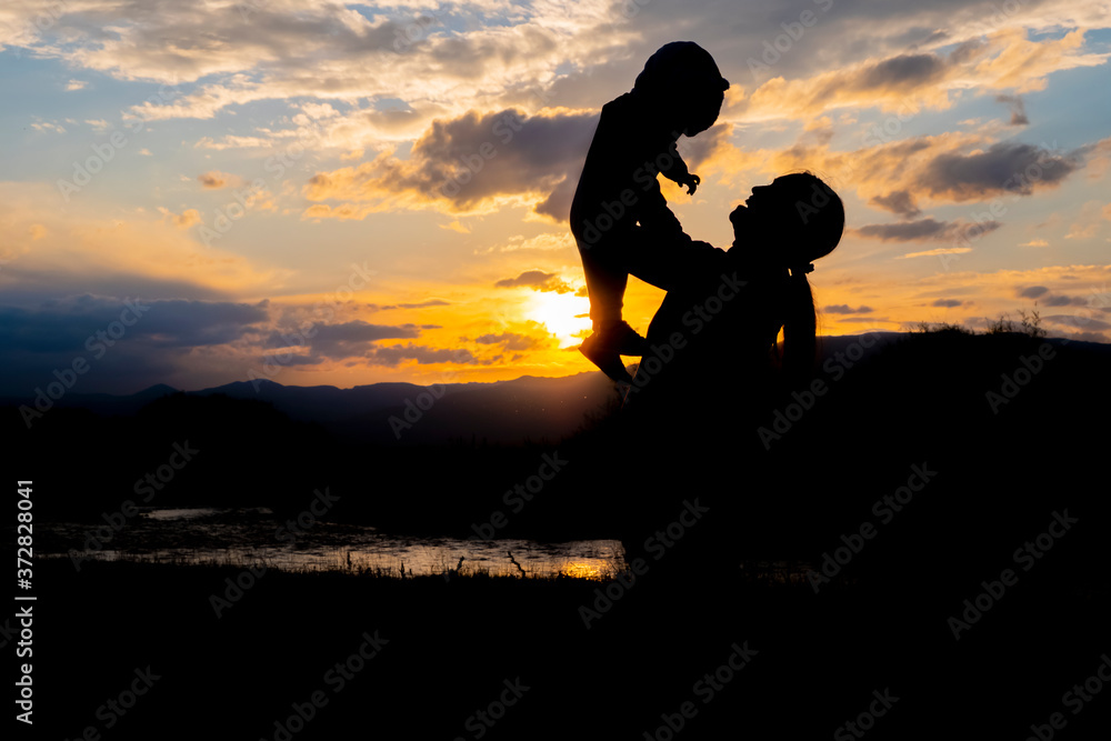 Silhouettes of mother with child on her hands with sunset and river background. Happy cheerful family. People lifestyle concept. Healthy lifestyle. Family recreation concept. Happy childhood concept.