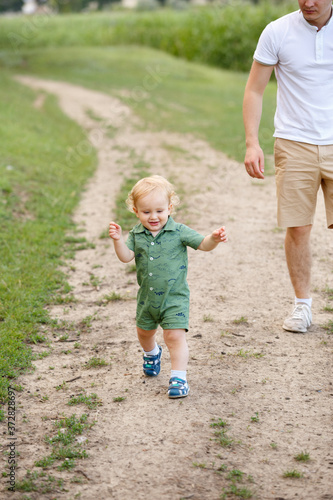 Cute little boy walking along the path on the background of reeds. His father is with him. Walk in park. Family life.
