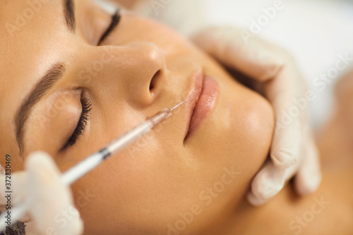 Hands of cosmetologist making botox injection in female upper lip with syringe