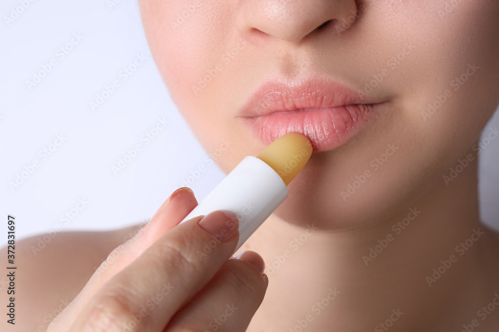Naklejka premium Woman applying hygienic lipstick on lips against white background, closeup