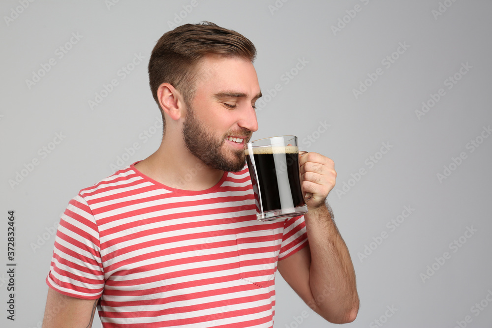 Handsome man with cold kvass on light grey background. Traditional Russian summer drink Handsome man with cold kvass on light grey background. Traditional Russian summer drink
