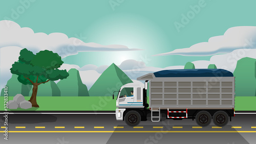 Traveling of cargo tipper truck on the asphalt road. with environment of green meadow and mountain at area outside the community area.
