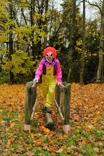 Halloween holiday. Evil clown in  overalls and in a scary mask on the playground in the autumn park.Autumn holidays time. halloween mood.Carnival in October