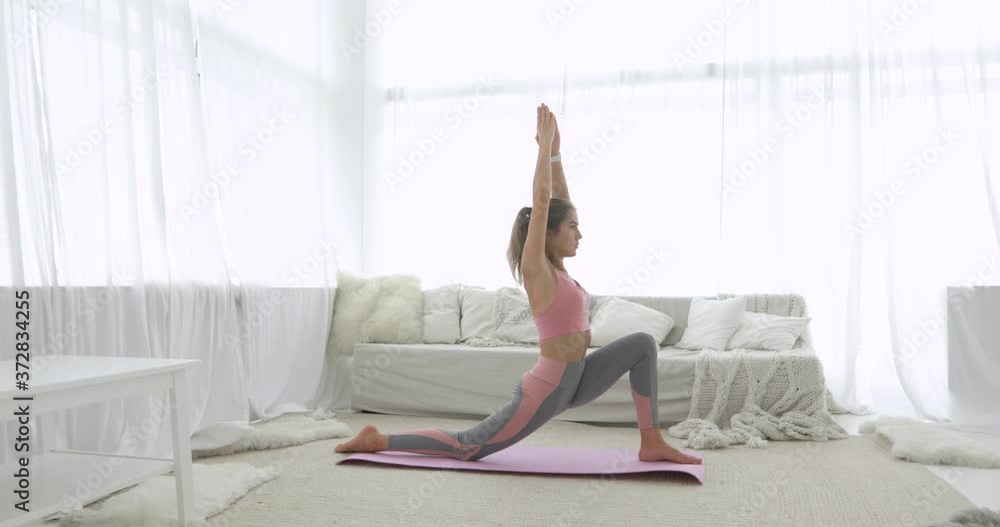 Girl is stretching her legs making physical exercise. Athletic young woman is doing lunge warrior yoga pose in living room at home, side view. Fitness, yoga practice, workout and wellness concept. Girl is stretching her legs making physical exercise. Athletic young woman is doing lunge warrior yoga pose in living room at home, side view. Fitness, yoga practice, workout and wellness concept.