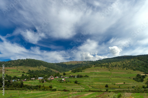 Mountain summer day landscape with clouds on blue sky, river and small houses.