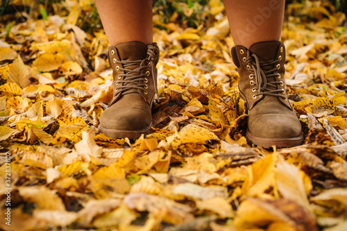 Close up photo of someone's feet in classic leather boots standing on the ground with yellow autumn leaves © honey_inside