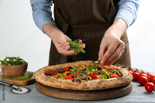 Woman adding arugula to vegetable pizza at table, closeup