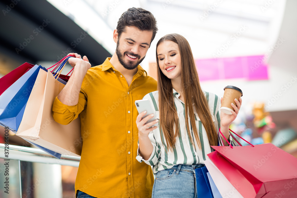 Portrait of two people man woman have break pause use smartphone check boutique retail off-sales notification hold coffee take-away cup many packages in shopping mall aisle Portrait of two people man woman have break pause use smartphone check boutique retail off-sales notification hold coffee take-away cup many packages in shopping mall aisle