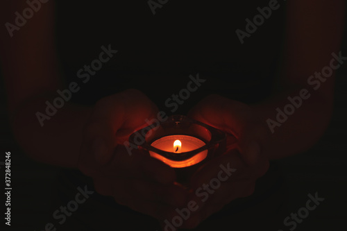 Person holding burning candle in darkness, closeup
