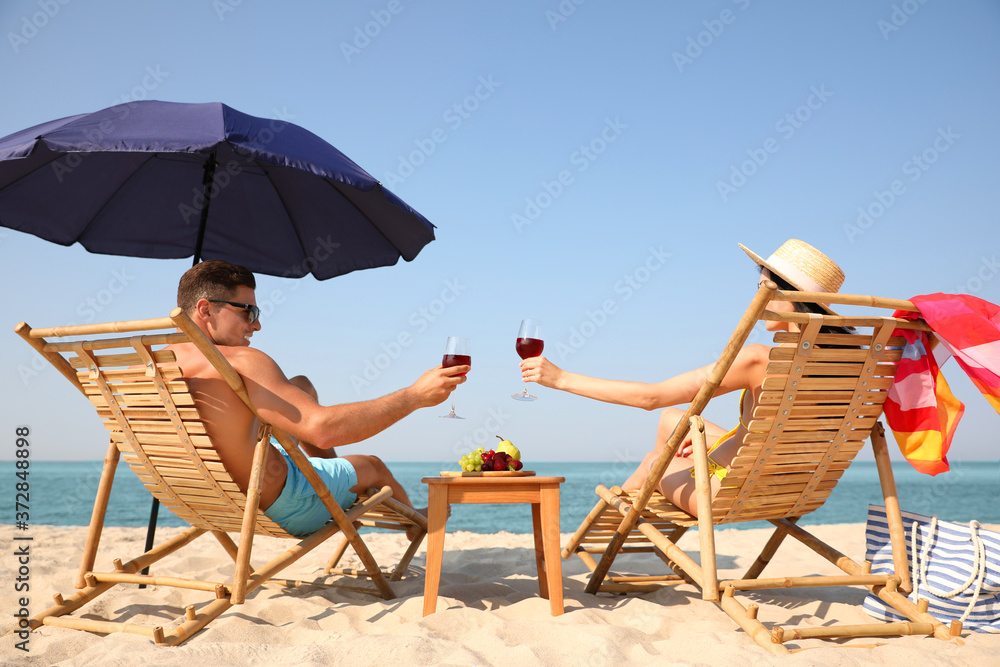Happy couple with wine on sunny beach at resort