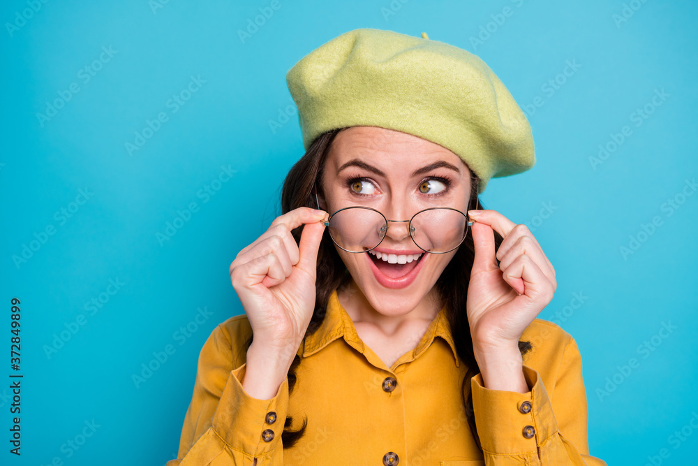 Close up photo of astonished positive cheerful girl look copyspace touch specs impressed season bargain information wear yellow shirt headwear isolated over blue color background Close up photo of astonished positive cheerful girl look copyspace touch specs impressed season bargain information wear yellow shirt headwear isolated over blue color background
