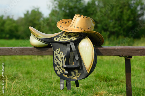 The horse saddle and cowboy hat are outdoors.