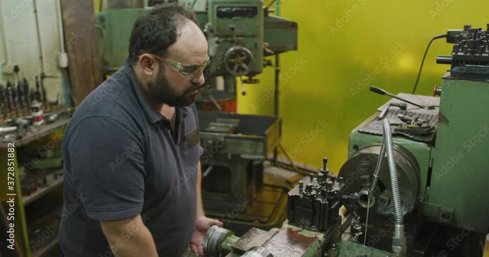 Caucasian male factory worker at a factory sitting at a workbench and operating machinery Caucasian male factory worker at a factory sitting at a workbench and operating machinery