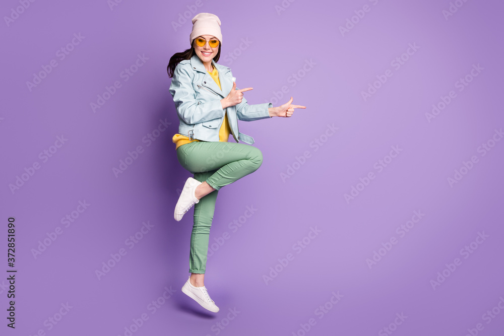 Full length photo positive girl promoter jump point index finger copyspace present ads promotion recommend suggest select wear yellow green headwear sunglass isolated violet color background
