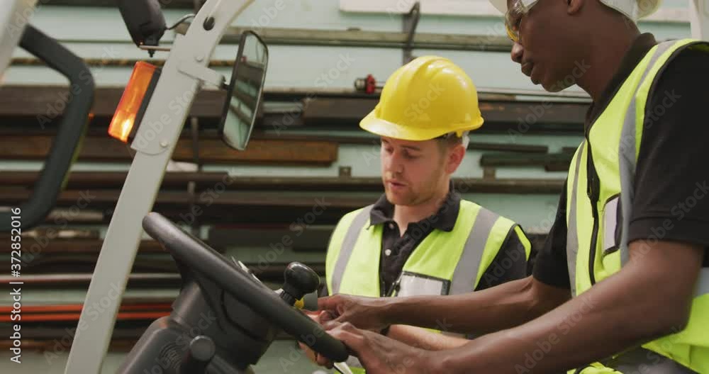 An African American and a Caucasian male factory worker at a factory talking in a warehouse area An African American and a Caucasian male factory worker at a factory talking in a warehouse area