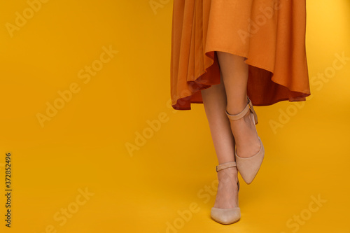 Woman wearing stylish shoes on yellow background, closeup. Space for text