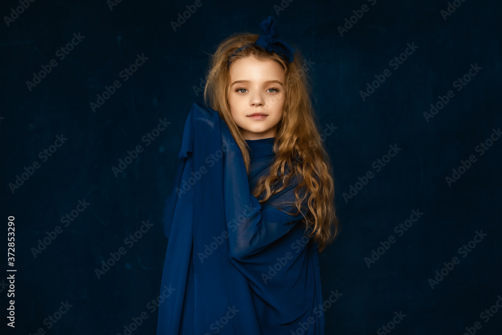 Art Portrait of Beautiful young girl with blonde curly long hair, holding her hands at her face on blue background Art Portrait of Beautiful young girl with blonde curly long hair, holding her hands at her face on blue background