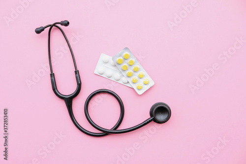 Black modern stethoscope and tablets on pink background.