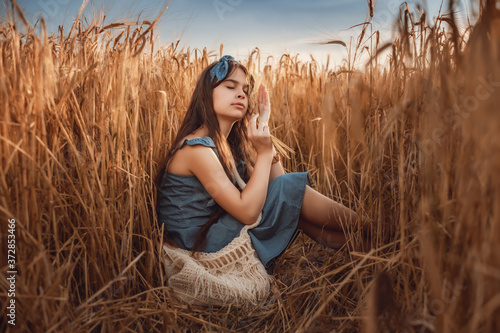 Portrait of Little girl 10-12 years old with long brown hair, walk in a wheat field on a summer evening