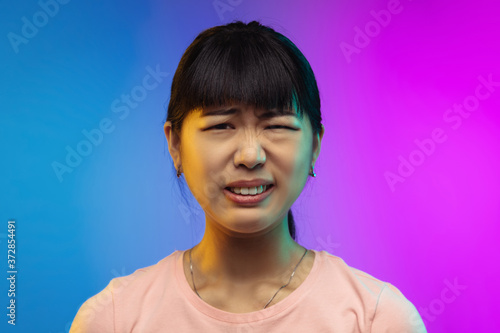 Disguasted. Close up asian young woman's portrait isolated on gradient studio background in neon. Beautiful female model in casual style. Concept of human emotions, facial expression, youth, sales, ad