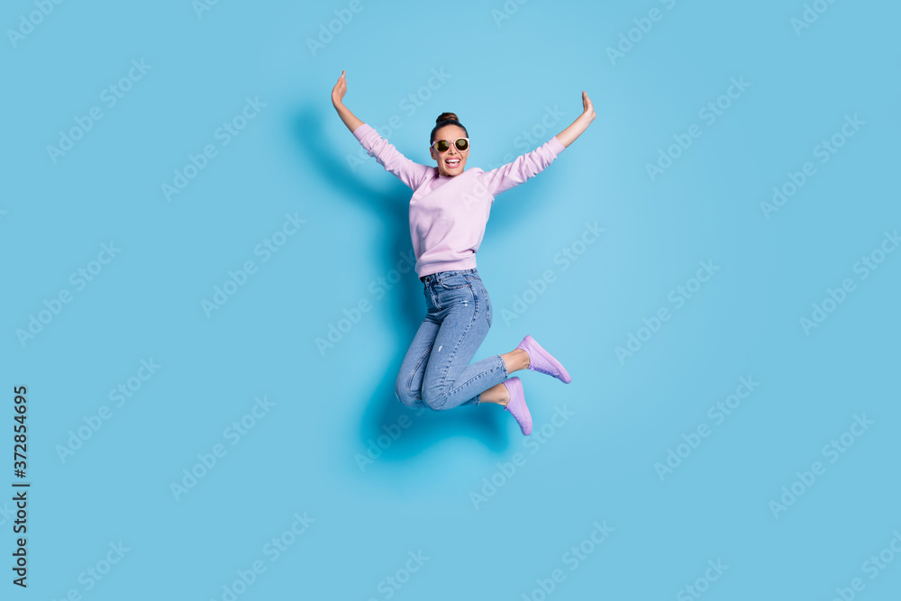 Full length photo of cheerful candid energetic girl jump enjoy weekend raise hands wear good look pullover isolated over blue color background