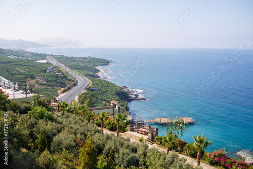 An empty asphalt road winds along the breathtaking scenic coastline on a sunny summer day. A spectacular shot of a coastal road overlooking clear blue skies and the calm Mediterranean Sea.