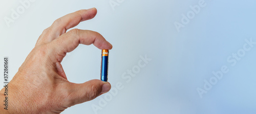 Man's hand holding small AAA battery between thumb and index finger